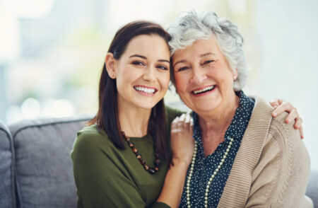 A young woman poses next to a senior woman as they share a warm embrace.