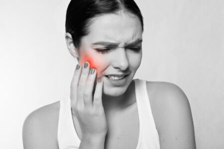 Black-and-white photo of a woman wincing in pain as she touches her right cheek. Red shading indicates the area in her jaw that is in pain.