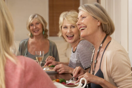 A group of senior women smile and laugh over dinner.