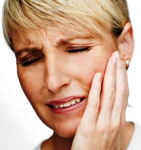 A woman winces in pain while holding her left cheek.