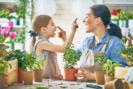 A mom and daughter touch each other's noses while working with plants.